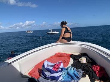 A snorkeler enjoys the ocean while sitting on the edge of a boat, with other boats and swimmers visible in the background — a perfect day for water activities.