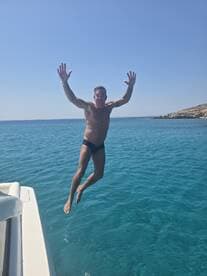 A man joyfully leaps off the side of a boat into the crystal-clear ocean, capturing the thrill of summer adventures on the water.