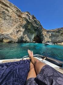 A person relaxes on the deck of a boat, enjoying the stunning turquoise waters and rocky cave formations — a perfect scene for a day of leisure on the water.