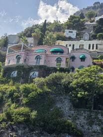 A picturesque view of a colorful villa perched on a hillside, surrounded by lush greenery and scenic landscapes.