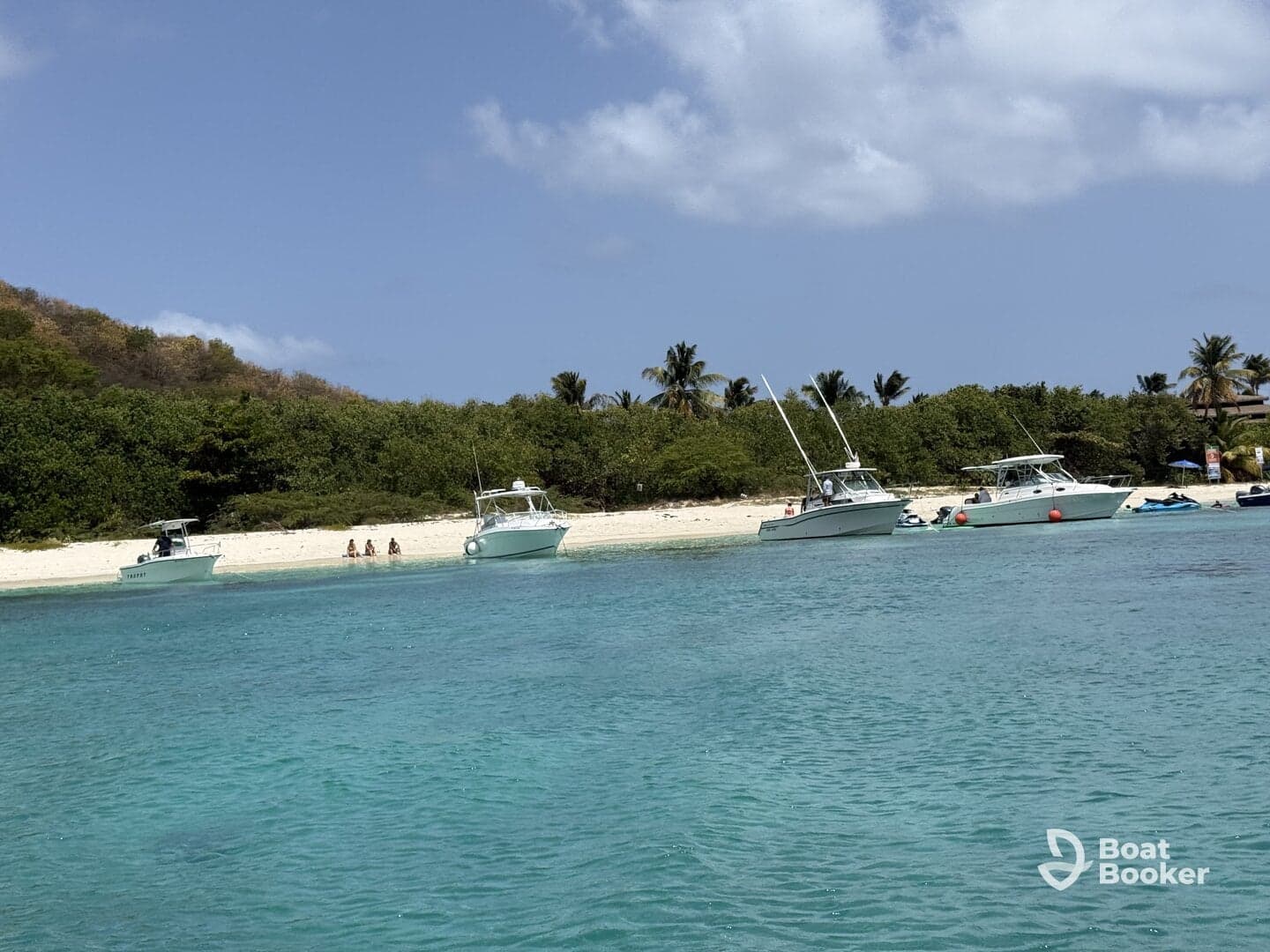 A scenic view of several boats anchored near a beach, with a group of people enjoying the sun and sand — perfect for a relaxing day on the water.