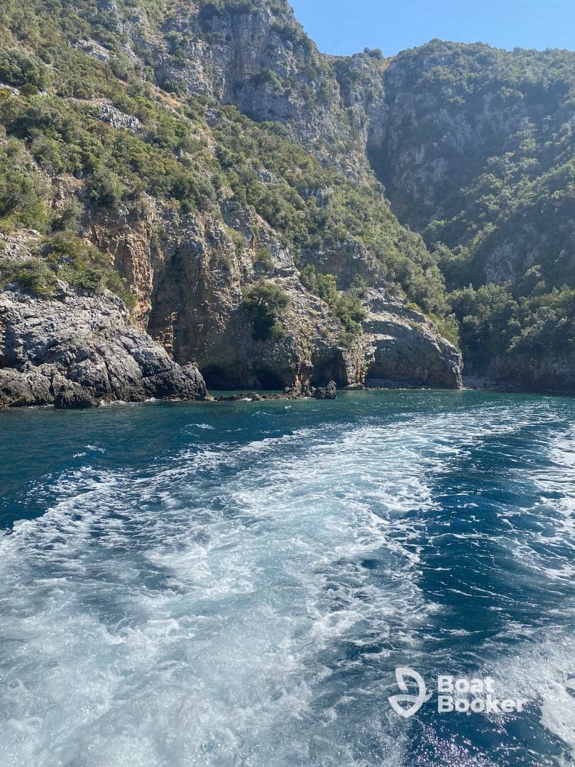 A stunning view of a rocky coastline with lush greenery, captured while cruising on the water, showcasing the beauty of nature and the thrill of boating adventures.