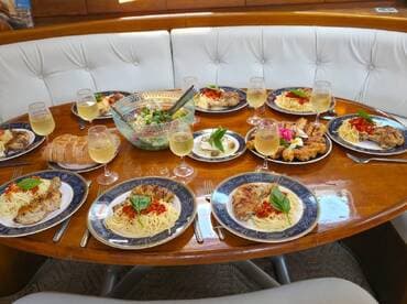 A beautifully arranged dining table on a boat featuring gourmet dishes, including pasta, grilled chicken, and fresh salad, perfect for a luxurious onboard dining experience.