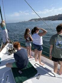 A group of friends and family enjoy a sailing trip, taking in the scenic views of the coastline while aboard a yacht.
