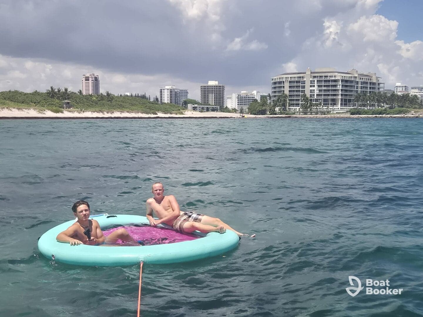 Two young men relax on a floating mat in the clear waters, enjoying a sunny day at the beach — a perfect scene for summer fun and water activities.