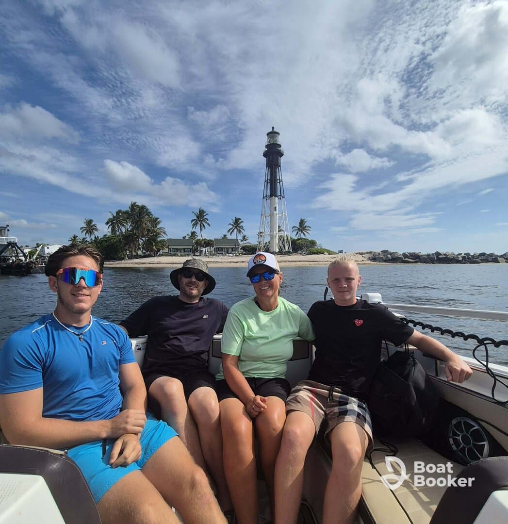 A cheerful group enjoys a day on the water, posing in front of a picturesque lighthouse — a perfect family outing under the sun.