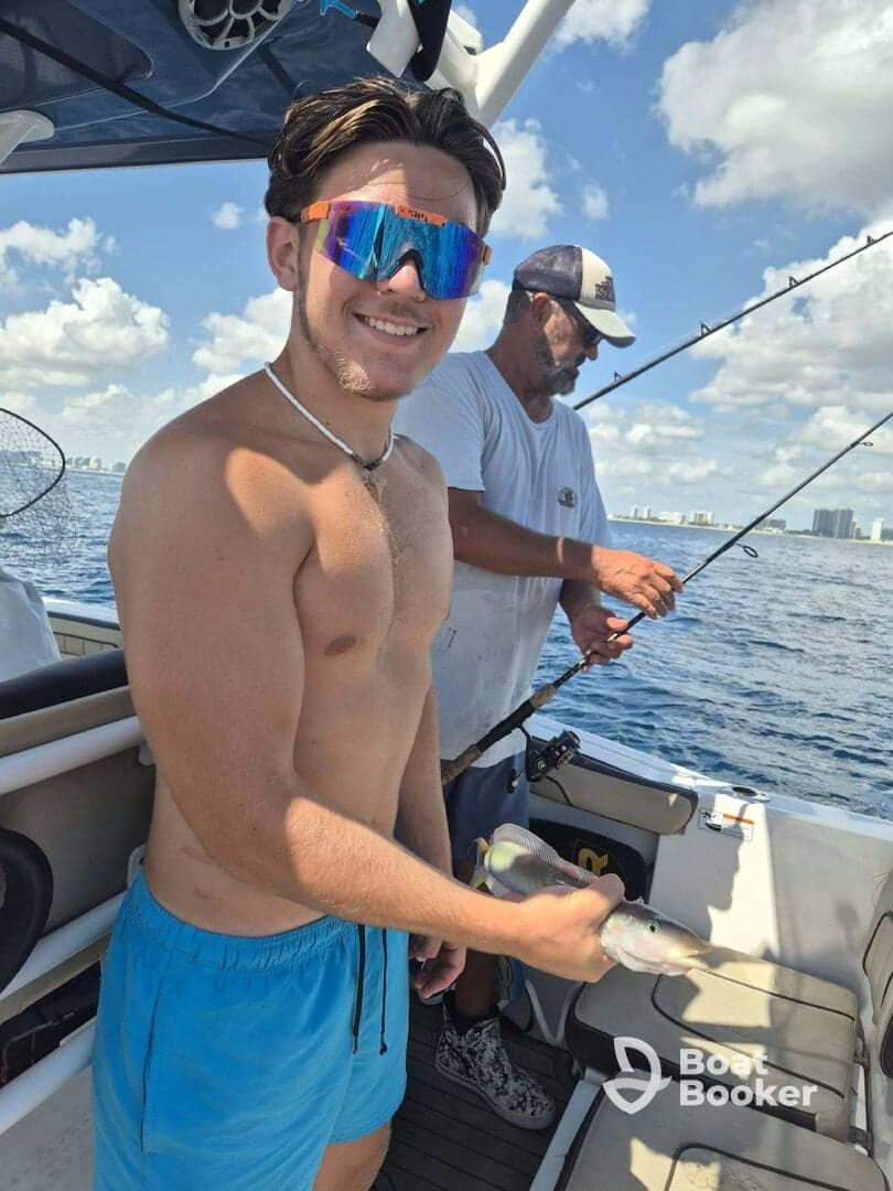 A young angler proudly displays his catch while fishing on a boat, showcasing the excitement of a day on the water with friends.