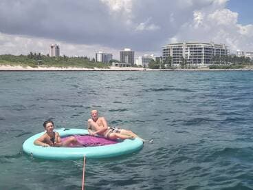 Two young men relax on a floating mat in the clear waters, enjoying a sunny day at the beach — a perfect scene for summer fun and water activities.