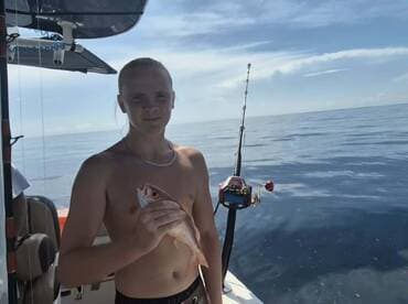 A young angler proudly displays his catch while fishing on the open ocean, capturing the thrill of a successful day at sea.