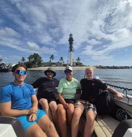 A cheerful group enjoys a day on the water, posing in front of a picturesque lighthouse — a perfect family outing under the sun.