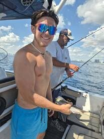 A young angler proudly displays his catch while fishing on a boat, showcasing the excitement of a day on the water with friends.