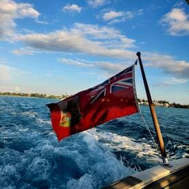 A vibrant shot of a boat's flag waving in the wind as it cruises through sparkling waters, showcasing the beauty of a day on the sea.