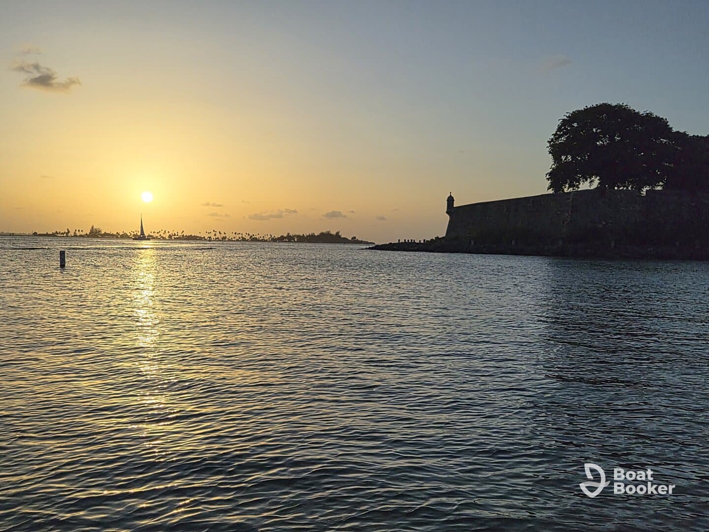 A stunning sunset view over the harbor, featuring a silhouette of a historic fort and a sailboat in the distance — perfect for capturing the beauty of coastal destinations.