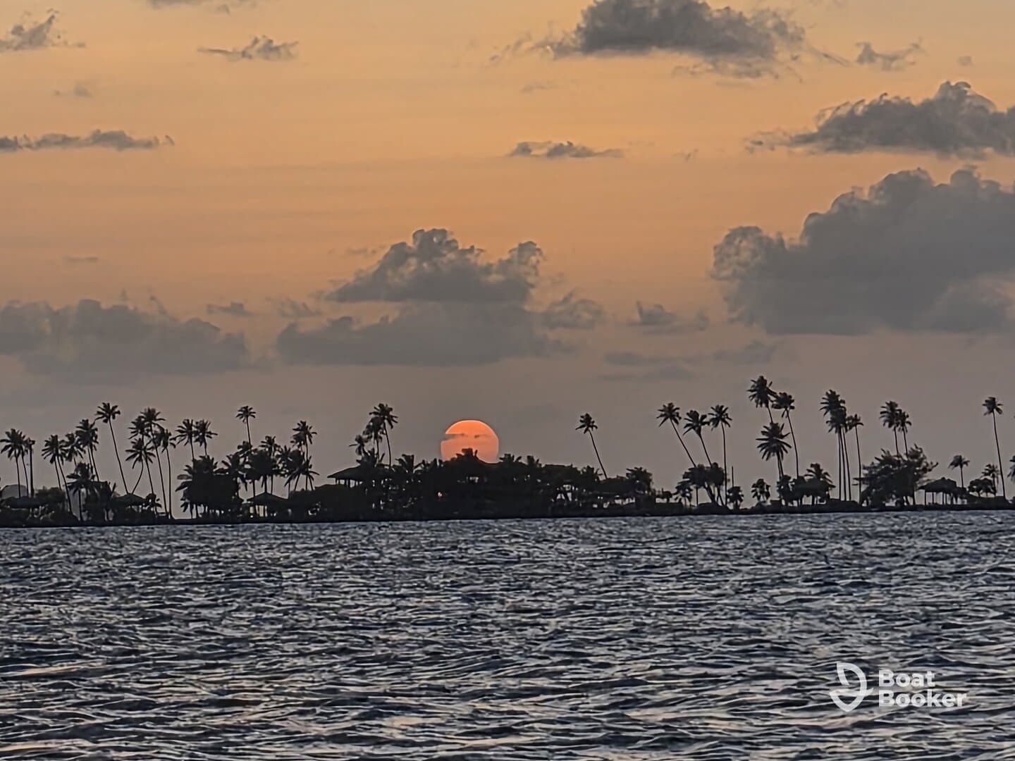 A stunning sunset over an island silhouette, framed by palm trees, creating a picturesque coastal scene perfect for romantic getaways or serene boat trips.