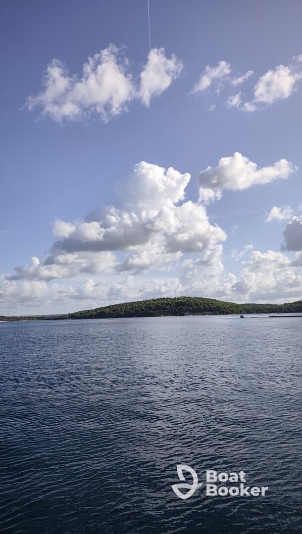 A scenic view of a calm water body with clouds overhead and a distant island, creating a tranquil atmosphere.