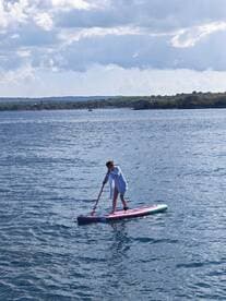 A woman enjoys paddleboarding on calm waters, showcasing the perfect blend of adventure and relaxation in a scenic outdoor setting.
