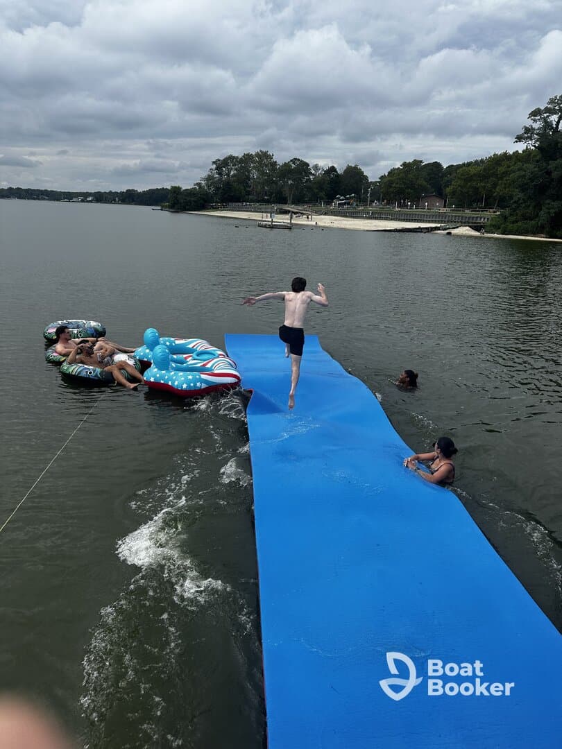 A lively scene of friends enjoying a day on the water, with one jumping off a floating platform while others relax on inflatable loungers — perfect for summer fun and water activities.