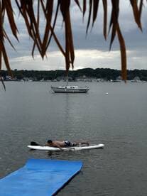 A man paddleboards in calm waters with a sailboat anchored in the background, showcasing a serene day on the water.
