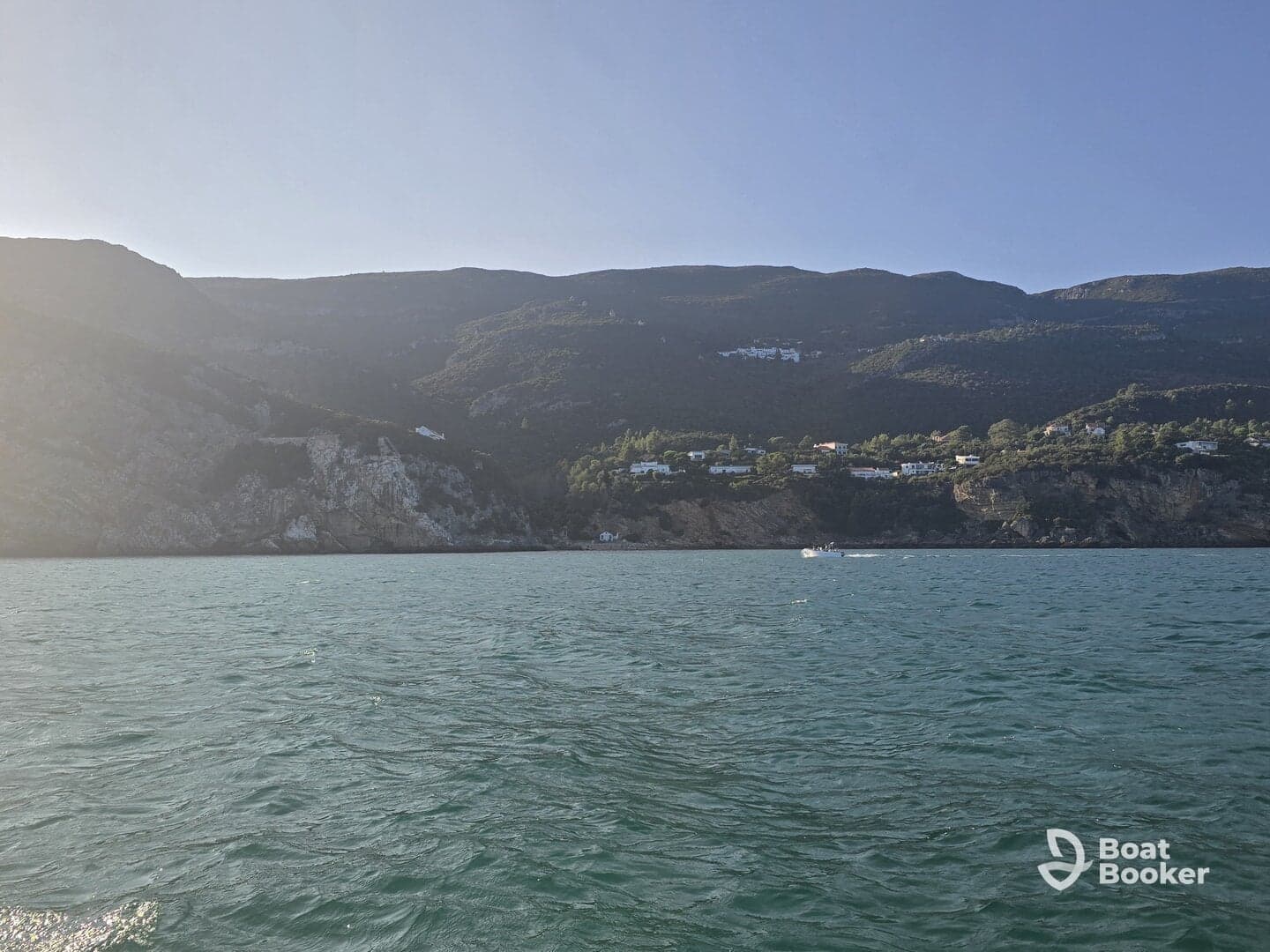 A stunning view of a rugged coastline with lush hills and scattered homes, perfect for showcasing the natural beauty of the area while enjoying a boat trip.
