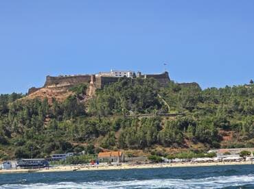 A stunning view of a historic fortress perched on a hillside, overlooking a beautiful beach and coastline — a perfect destination for sightseeing and exploration.