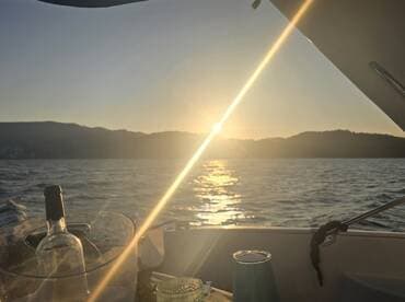 A serene sunset view from a boat, featuring a wine bottle and glass, creating a perfect ambiance for a relaxing evening on the water.