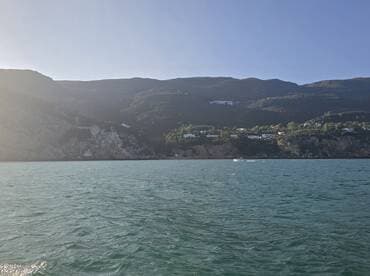 A stunning view of a rugged coastline with lush hills and scattered homes, perfect for showcasing the natural beauty of the area while enjoying a boat trip.