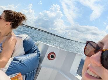 Two friends enjoy a sunny day on the water, capturing the fun of their boating experience with a picturesque pier in the background.