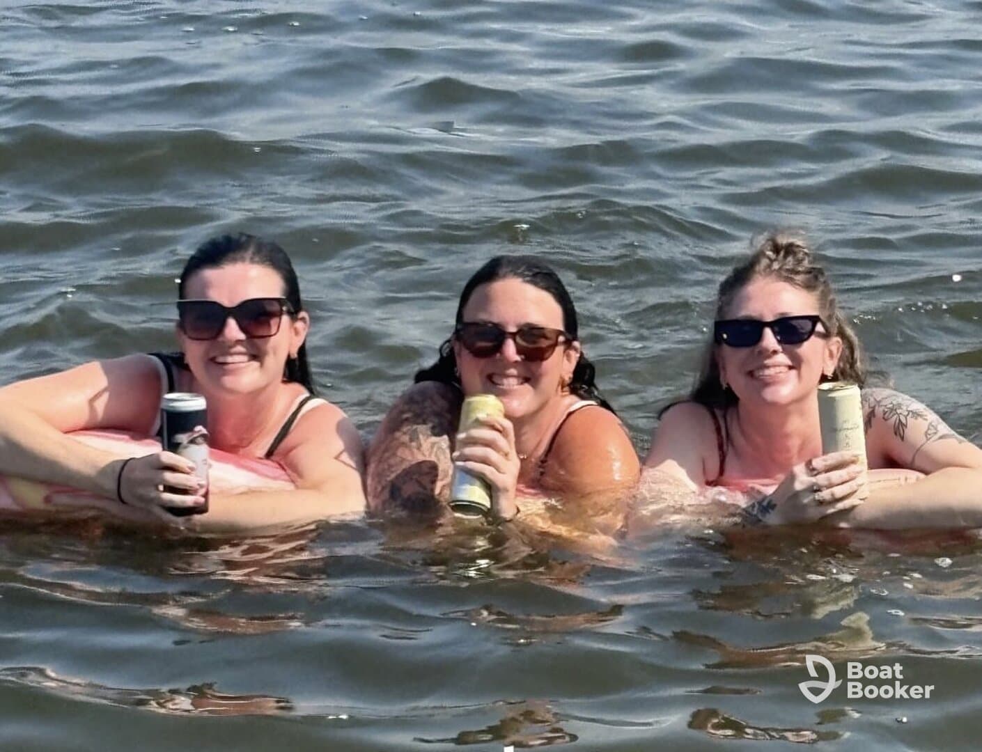 Three friends enjoy a fun day in the water, relaxing with drinks and floating on inflatable rings — perfect for summer parties and memorable outings.