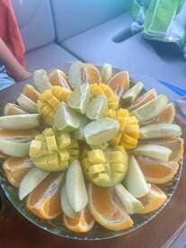 A vibrant fruit platter featuring a colorful assortment of mango, lime, apple, and orange slices, perfect for enjoying fresh snacks while on a boat trip.