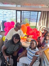 A joyful group celebrates a birthday aboard a boat, surrounded by colorful balloons and a delicious cake — perfect for memorable gatherings on the water.