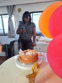 A woman stands in the cabin of a boat, checking her phone next to a beautifully decorated cake, perfect for celebrations on the water.