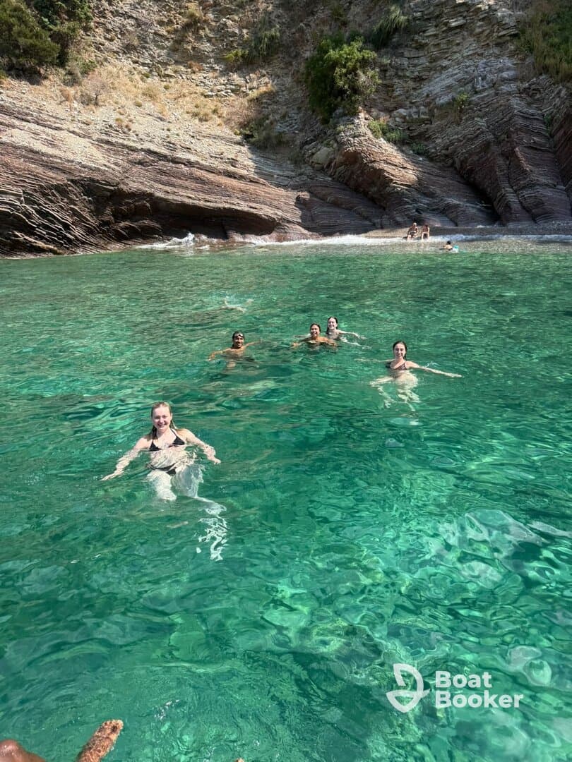 A lively group enjoys swimming in crystal-clear waters, surrounded by stunning rocky cliffs — a perfect day for beach fun and relaxation.
