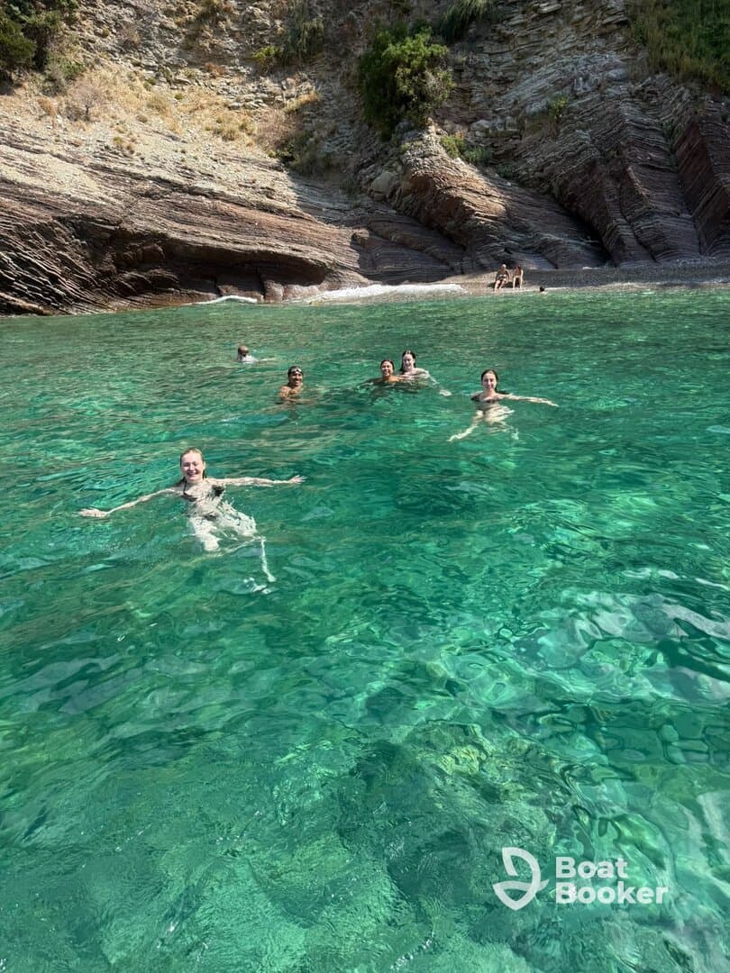 A lively group enjoys swimming in crystal-clear waters, surrounded by stunning rocky cliffs — a perfect day for beach fun and relaxation.