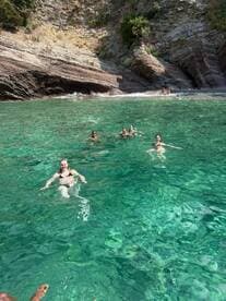 A lively group enjoys swimming in crystal-clear waters, surrounded by stunning rocky cliffs — a perfect day for beach fun and relaxation.