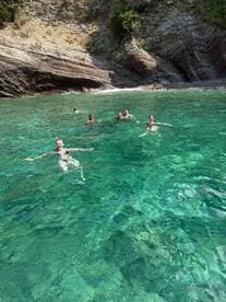 A lively group enjoys swimming in crystal-clear waters, surrounded by stunning rocky cliffs — a perfect day for beach fun and relaxation.