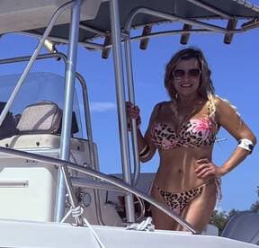 A woman poses on the deck of a boat, showcasing a vibrant bikini against a clear blue sky — perfect for summer outings and beach adventures.