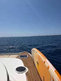 A clear view of a yacht's deck with a paddleboard visible, cruising through calm waters under a bright blue sky — perfect for summer adventures on the sea.