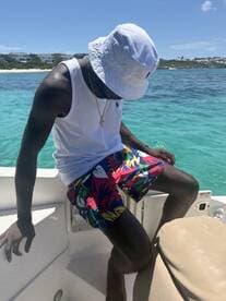 A man enjoys a sunny day on a boat, dressed in vibrant summer attire, with a beautiful beach backdrop — perfect for summer adventures on the water.