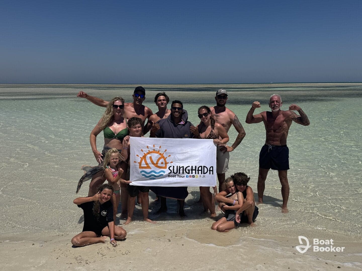 A joyful group poses on the beach holding a banner for Sunghada Boat Tours, celebrating their memorable day on the water with family and friends.