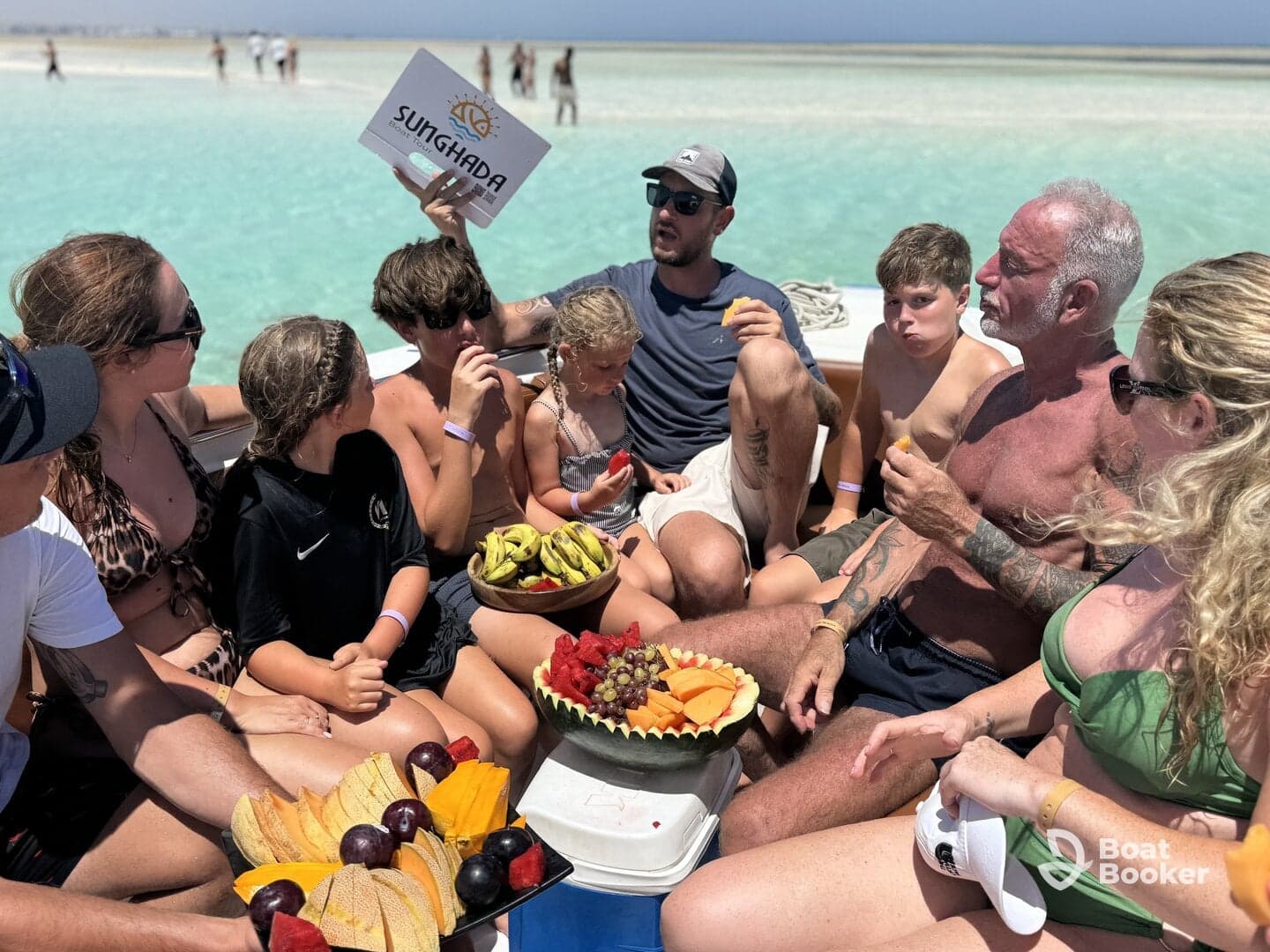 A lively group enjoys a variety of fresh fruits aboard a boat, creating a perfect beach day atmosphere with family and friends.