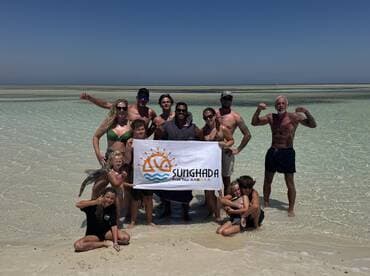 A joyful group poses on the beach holding a banner for Sunghada Boat Tours, celebrating their memorable day on the water with family and friends.