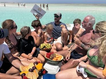 A lively group enjoys a variety of fresh fruits aboard a boat, creating a perfect beach day atmosphere with family and friends.