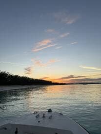 A serene sunset view from the bow of a boat, showcasing tranquil waters and a picturesque shoreline — perfect for evening cruises.