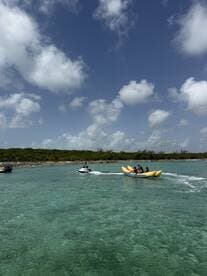 A thrilling scene of a group enjoying a banana boat ride while a jet ski speeds by in the clear turquoise waters, perfect for adventurous water activities.