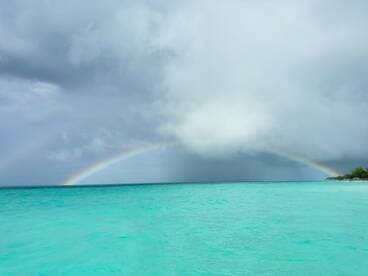 A stunning view of a vibrant rainbow arching over turquoise waters, creating a picturesque scene perfect for tropical getaways.