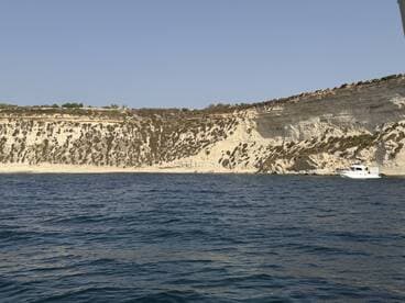 A picturesque view of a boat cruising along a stunning coastline, showcasing the natural beauty of the cliffs and clear waters.