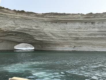 A stunning view of a natural rock arch along the coastline, showcasing the beauty of the surrounding waters — perfect for scenic boat tours.