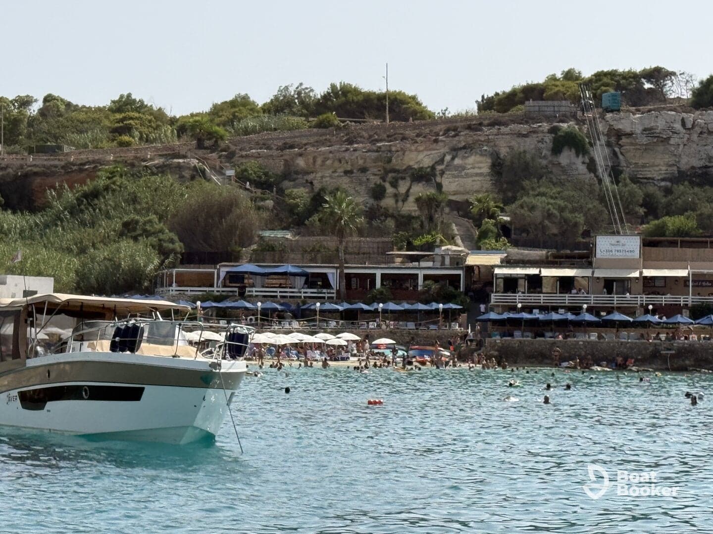 A scenic view of a boat anchored near a bustling beach, where guests enjoy swimming and sunbathing — a perfect summer getaway.