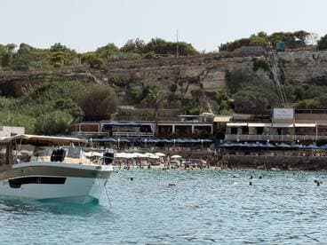 A scenic view of a boat anchored near a bustling beach, where guests enjoy swimming and sunbathing — a perfect summer getaway.