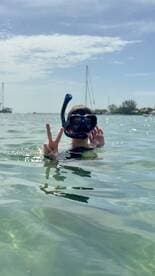 A child enjoys snorkeling in clear waters, flashing a peace sign while surrounded by a beautiful marine environment — a perfect moment for family adventures.